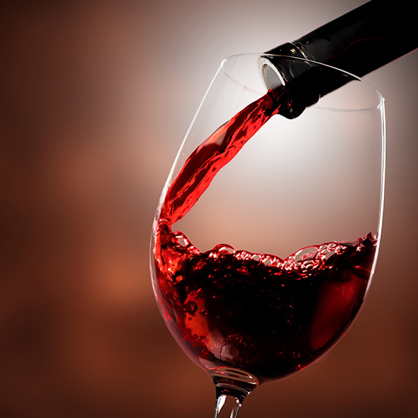 Alt text Wine glass filled with red wine, with a single drop falling into it.